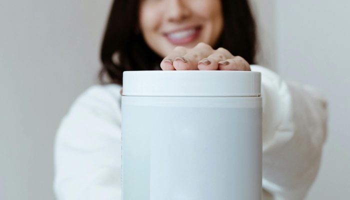 A cheerful woman presenting a container of health supplements against a minimalist background.
