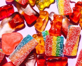 Colorful mix of gummy candies including bears and rainbow strips on a vibrant purple backdrop.
