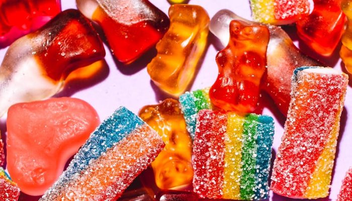 Colorful mix of gummy candies including bears and rainbow strips on a vibrant purple backdrop.